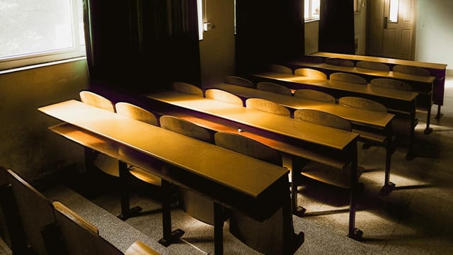 Sunlight streaming into an empty classroom with wooden desks and chairs in Hubei, China.