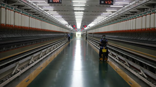 Long hallway in Indian textile factory with spinning machinery and workers.