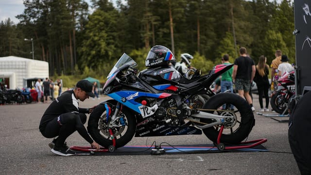 Man preparing sports motorcycle for race, with team support outdoors.