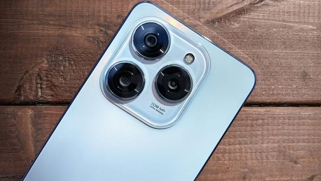 Close-up of a smartphone camera showing three lenses on a rustic wooden background.