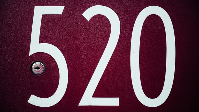 Close-up image of a red residential door with the number 520 and a keyhole.