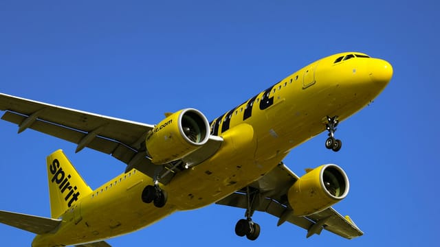 A vivid yellow commercial airplane in flight against a clear blue sky, showcasing dynamic travel and aviation.