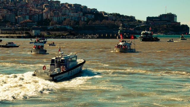 Multiple patrol boats navigate a scenic harbor, showcasing coastal urban life under clear skies.