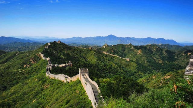 Stunning aerial view of the Great Wall of China winding over lush green hills under a clear blue sky.