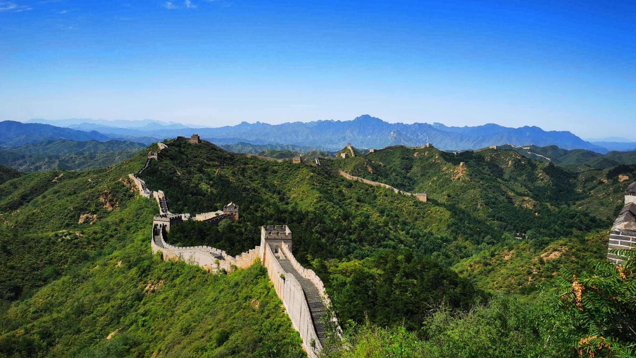 Stunning aerial view of the Great Wall of China winding over lush green hills under a clear blue sky.