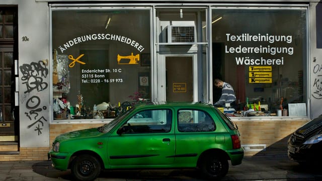 A green car parked outside a tailor shop in Bonn, Germany.