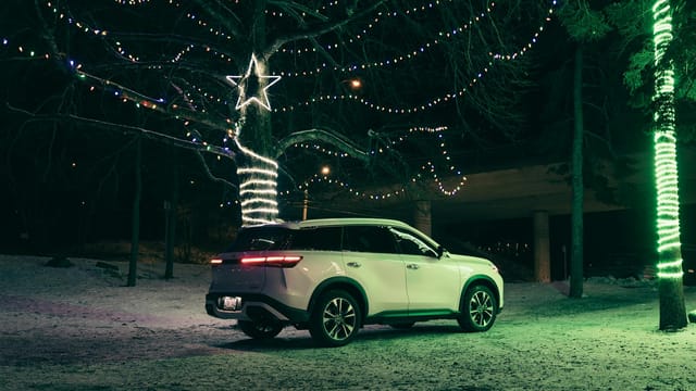 A white SUV parked in a snowy landscape adorned with festive Christmas lights at night.