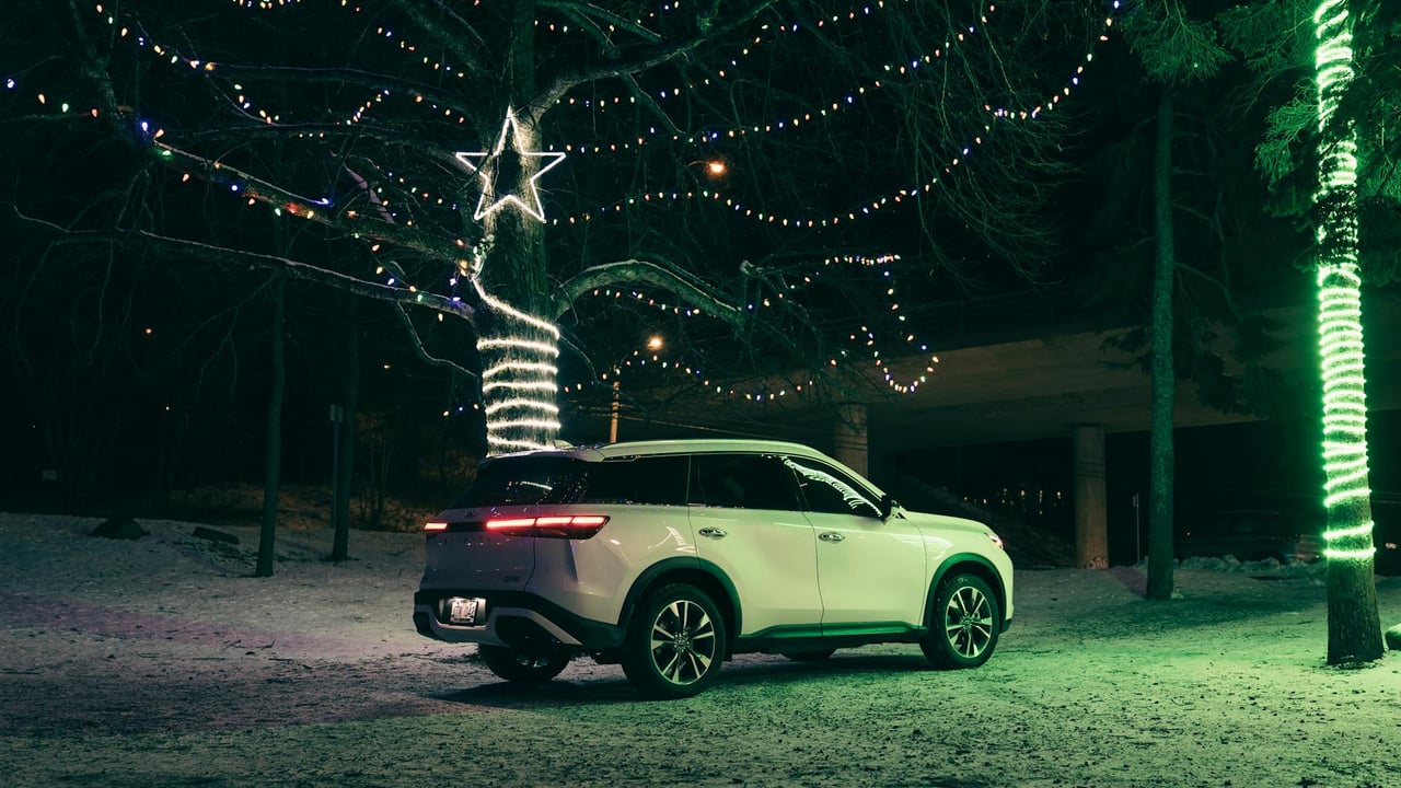 A white SUV parked in a snowy landscape adorned with festive Christmas lights at night.