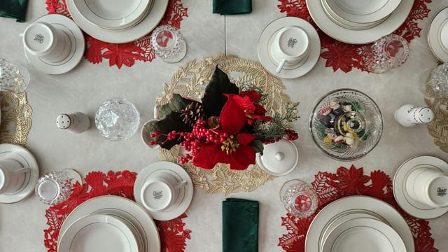 Top view of a beautifully set Christmas dinner table with porcelain plates and a vibrant floral centerpiece.