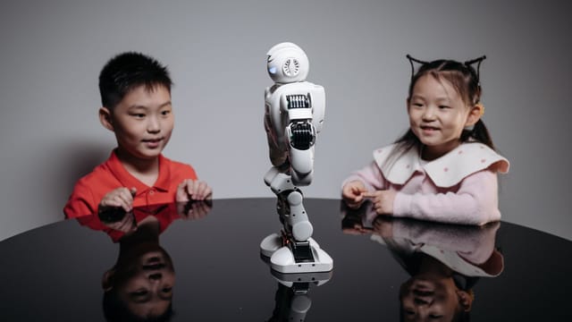 Two children fascinated by a small humanoid robot indoors on a table.
