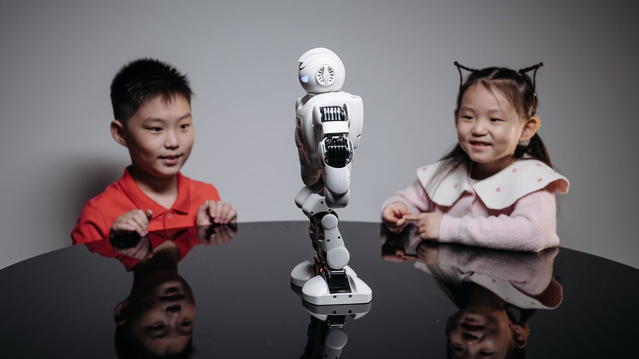 Two children fascinated by a small humanoid robot indoors on a table.
