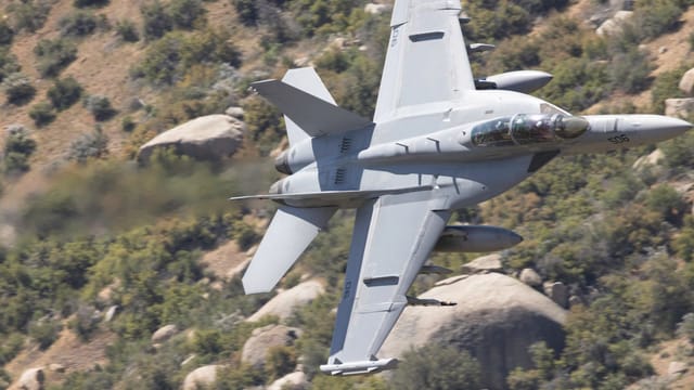 F-18 Super Hornet flies low over Kernville, California, showcasing speed and agility amidst rugged terrain.