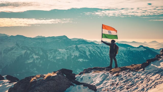 Man holding Indian flag atop a scenic snowy mountain range, capturing nature's beauty.