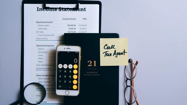 Top view of a desk with income statement, phone calculator, and tax reminder note.