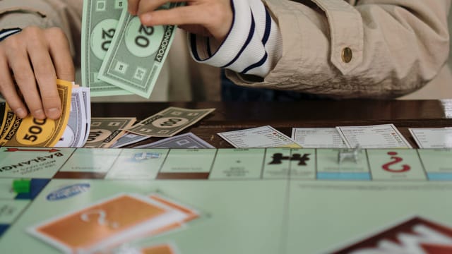 Hands counting Monopoly money during a board game session, highlighting fun and strategy.