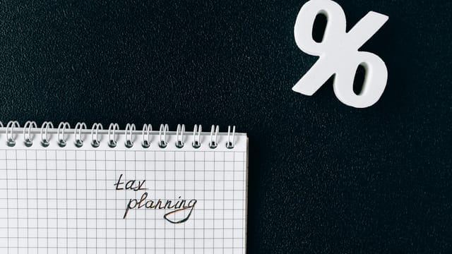 A notebook with 'tax planning' written on a grid paper next to a percent symbol on a black background.