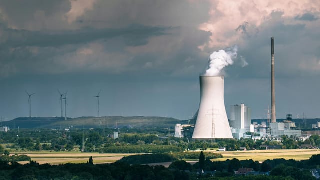 Aerial view of a power plant with steam rising, set against a dramatic sky in Duisburg, Germany.