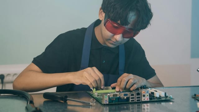 Young technician working with precision on a circuit board, demonstrating focused attention and technical skill indoors.