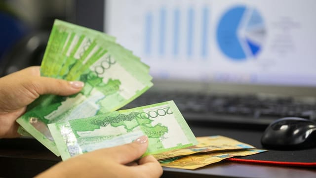 Hands counting cash with financial charts in background, indicating business or finance theme.