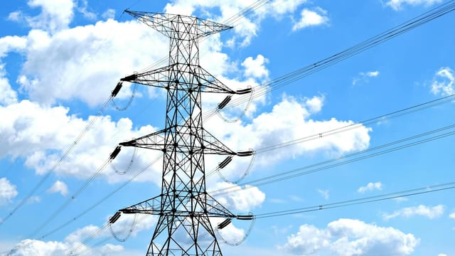 Electricity pylon with high voltage lines set against a vibrant blue sky with clouds.