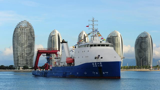 A modern cruise ship docked in the picturesque Sanya Bay, with iconic skyscrapers in the background.
