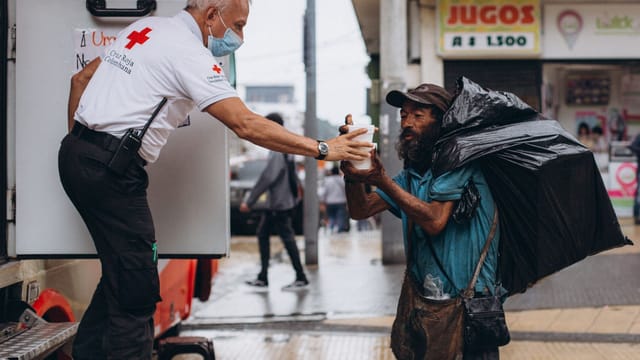 Red Cross worker assisting a homeless man outdoors with kindness.
