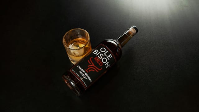 A bottle of Ole Bison Straight Bourbon Whiskey with a glass on a dark surface, New Orleans.