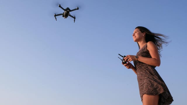 A woman enjoying flying a drone outdoors under a clear blue sky.