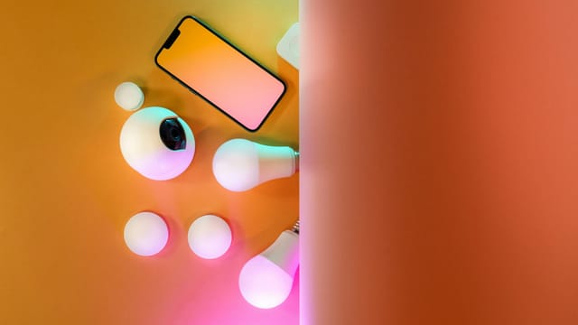 Top view of smart home gadgets including smartphone, camera, and light bulbs in a colorful setup.