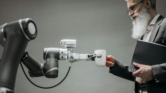 An elderly man receives a cup from a robotic arm in a modern office setting.
