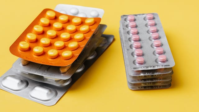 Heaps of various medication pills of different color and shape in blister packs placed on bright yellow background