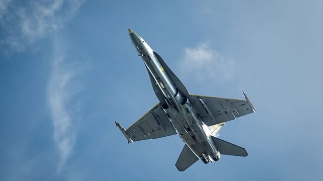 High-angle view of a military jet flying under a clear blue sky, showcasing its structure.