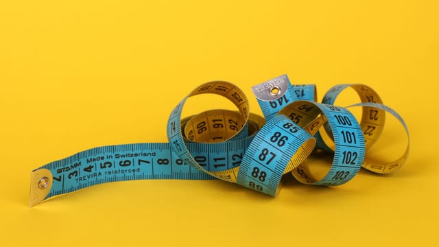 Colorful measuring tape curled up on a vibrant yellow background, ideal for design concepts.