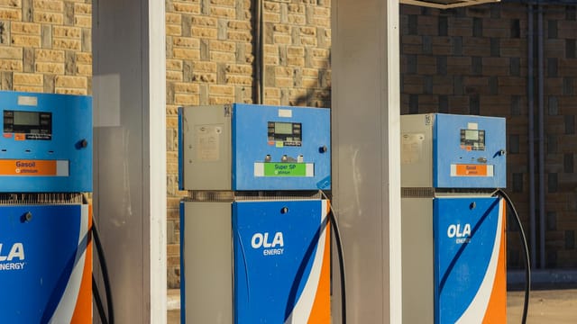 Three blue OLA Energy gas pumps at an outdoor station on a sunny day.