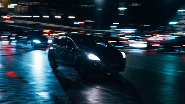 Illustrative image: Blurred cars and city lights create a dynamic nighttime urban scene, showcasing motion and energy.