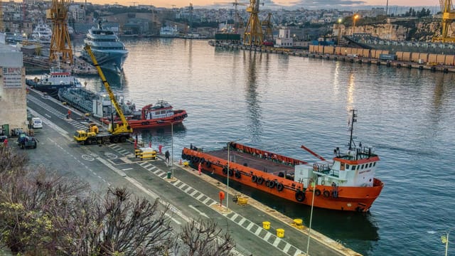 Vibrant sunset view of ships, cranes, and docks in a Maltese harbor.