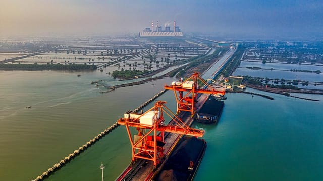 Stunning aerial view of a bustling industrial port in Banten, Indonesia with cranes and cargo ships.