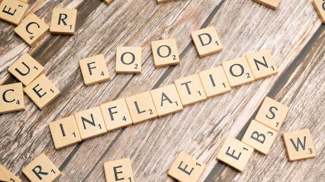 Wooden scrabble tiles arrange to spell 'Food Inflation' on a rustic wooden surface, conceptually depicting rising food prices.
