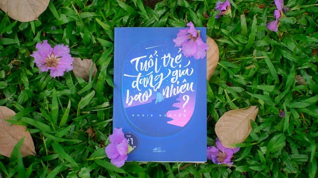 A book lying on green grass surrounded by purple flowers and dry leaves, creating a vibrant scene.
