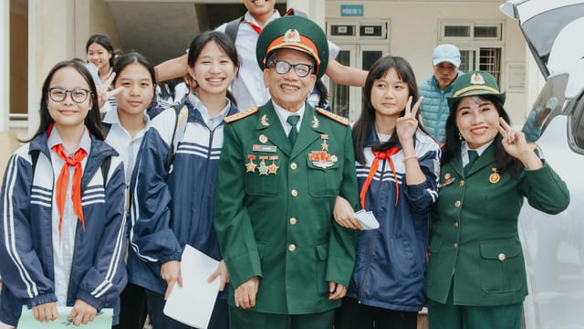 A group of smiling students posing with military veterans during a school event outdoors.