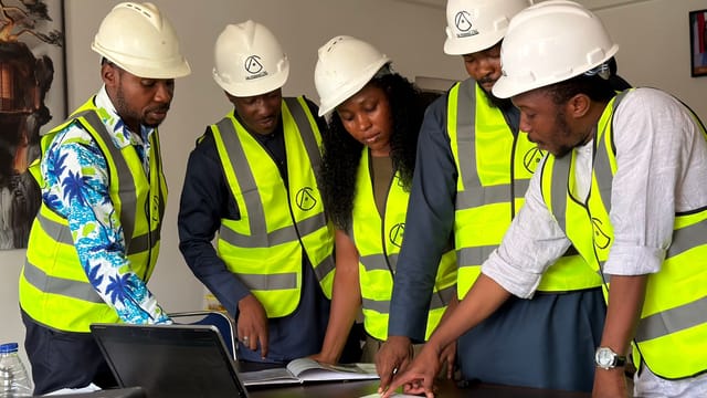 Group of engineers in safety gear reviewing blueprints indoors.