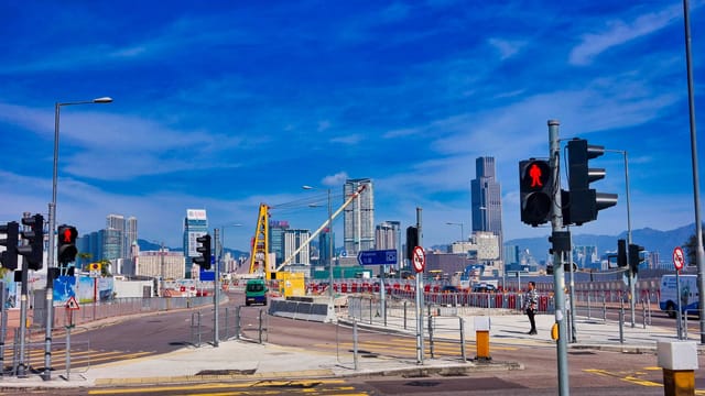 Dynamic view of Hong Kong's skyline featuring skyscrapers, roads, and traffic lights on a sunny day.