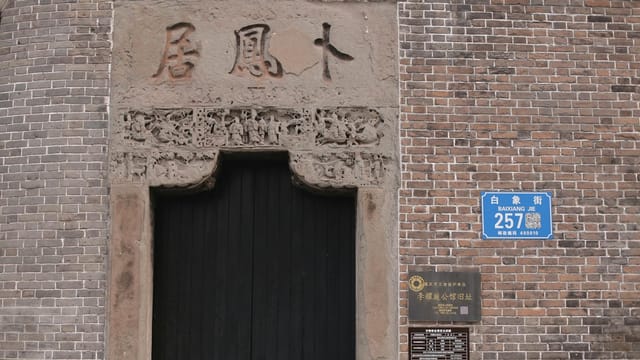 A close-up of a brick wall with intricate Chinese carvings and an address plaque in Baixiang Jie.