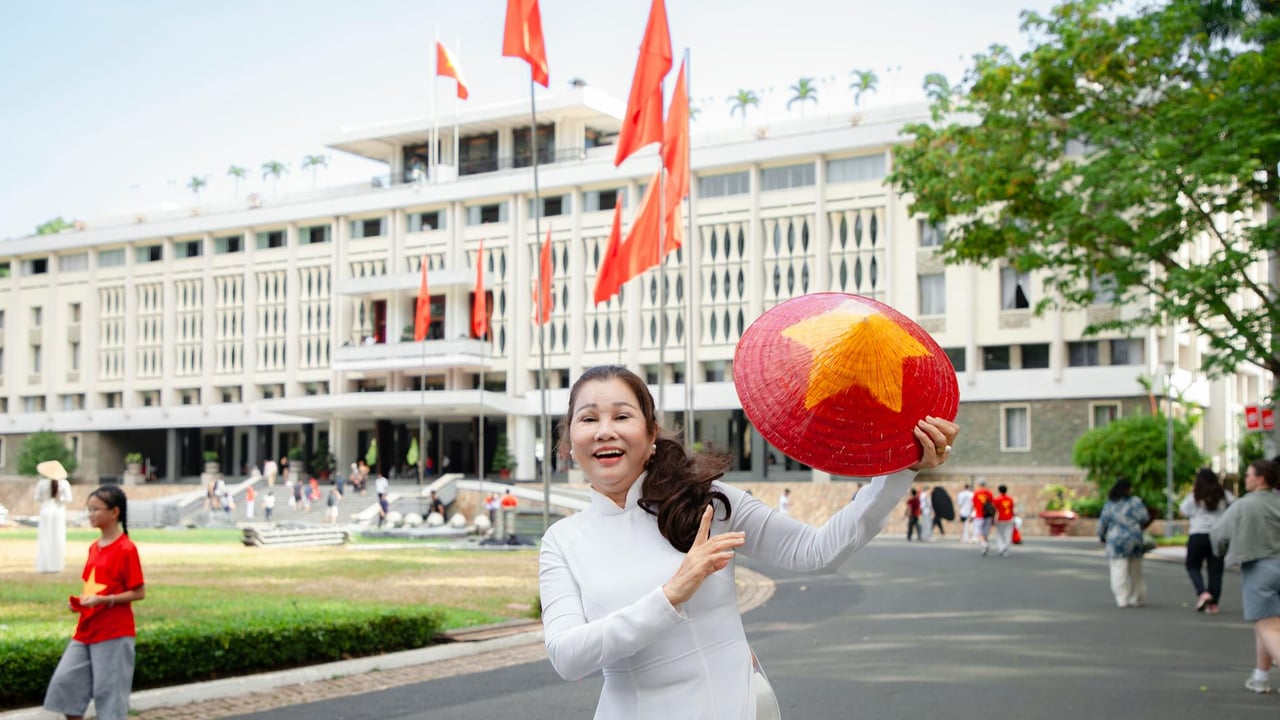 Smiling woman in traditional dress holds a Vietnamese star hat in front of a famous landmark.