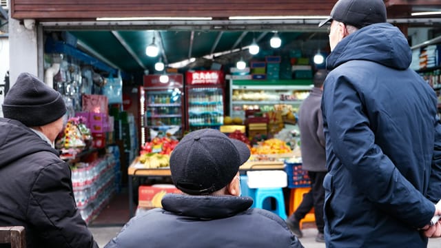Group of people wearing winter coats outside a bustling urban market.