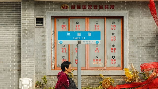 An outdoor urban scene featuring a person walking past an ornate building with a street sign in Chinese characters.