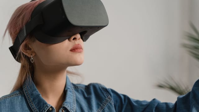A young woman in a denim jacket enjoying virtual reality indoors, experiencing immersive technology.