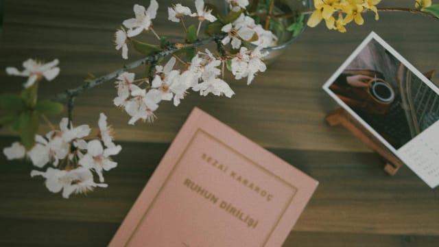 Flat lay of a book with cherry blossoms and a photo on a wooden table, creating a serene and artistic composition.
