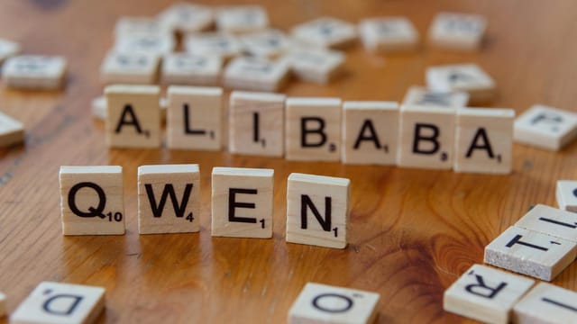 Close-up of Scrabble tiles spelling 'Alibaba' and 'Qwen' on a wooden surface.