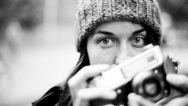Black and white portrait of a woman holding a vintage camera, showcasing her stylish personality.